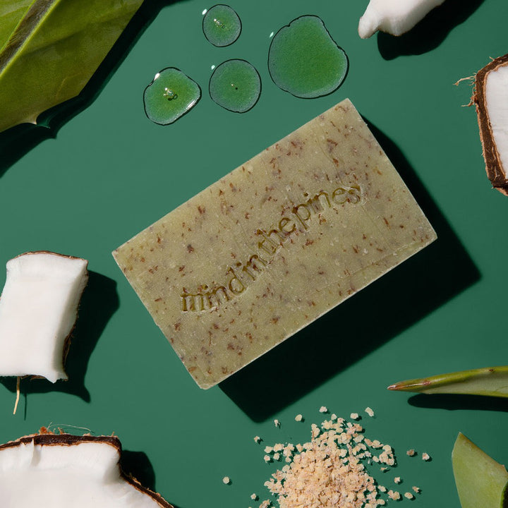 Jackfir Bushwhacker Bar Soap with visible wheat bran specks surrounded by water droplets, coconut pieces, and leaves