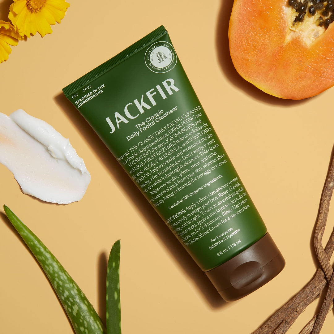 Jackfir Classic Daily Facial Cleanser green tube lying flat with white cream dollop, papaya, aloe, and yellow flowers