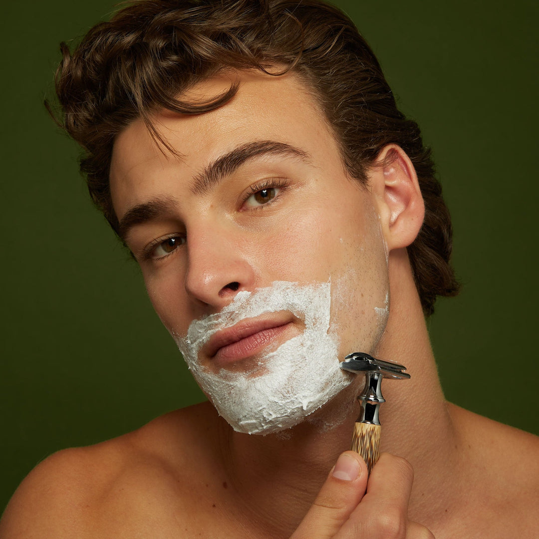 Man holding safety razor with Jackfir Classic Shave Cream lathered on lower face and jaw