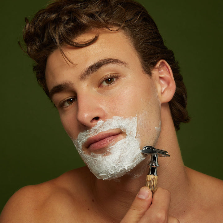 Man holding safety razor with Jackfir Classic Shave Cream lathered on lower face and jaw
