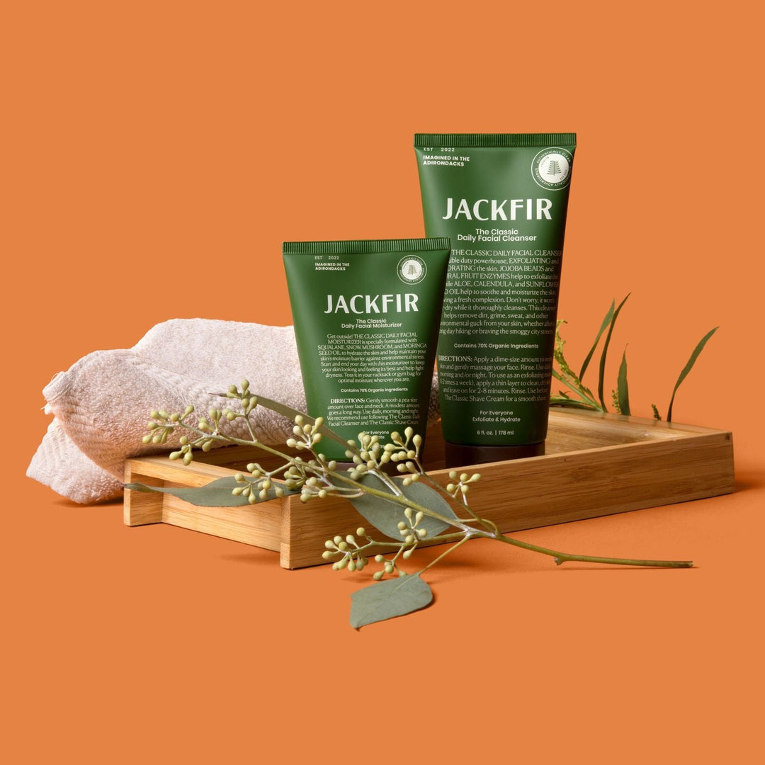 Jackfir Cleanser + Moisturizer Duo green tubes displayed on wooden platform with folded towel and eucalyptus sprigs