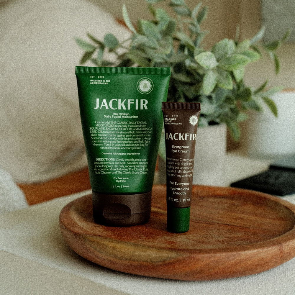 Jackfir Moisturizer + Eye Cream Duo tubes standing on wooden tray with greenery in background