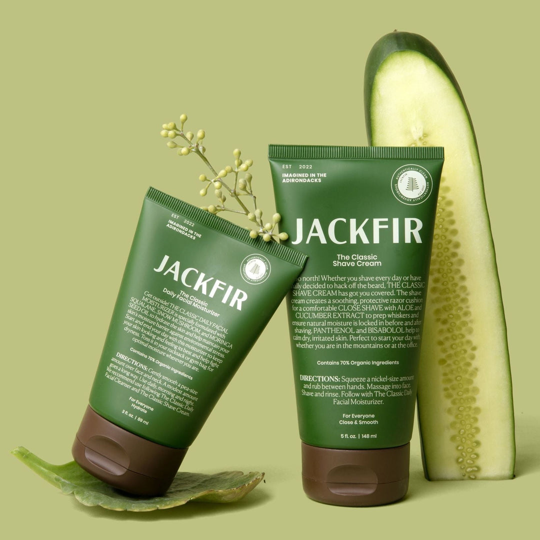 Jackfir Shave Cream + Moisturizer Duo green tubes standing upright with sliced cucumber and aloe leaf props