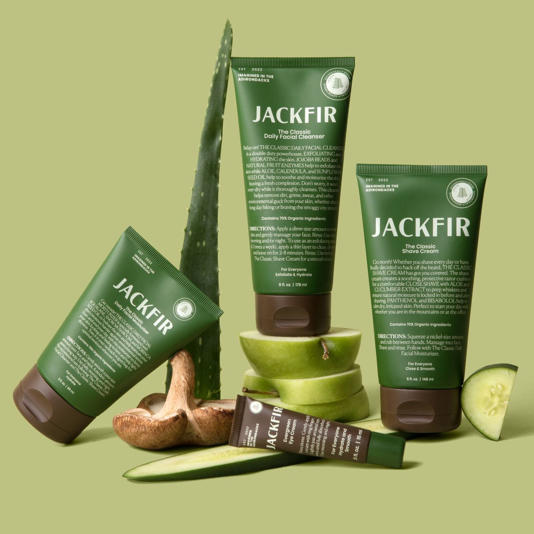 The Complete Jackfir Skincare Set displayed with green tubes, brown jars, aloe leaf and cucumber slice props