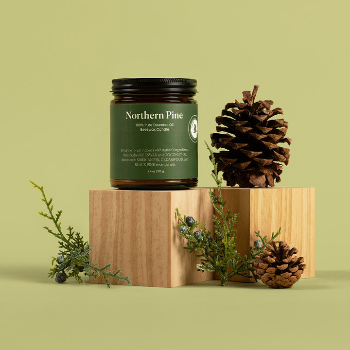 Northern Pine essential oil jar with pine cones and greenery on a wooden block against a green background