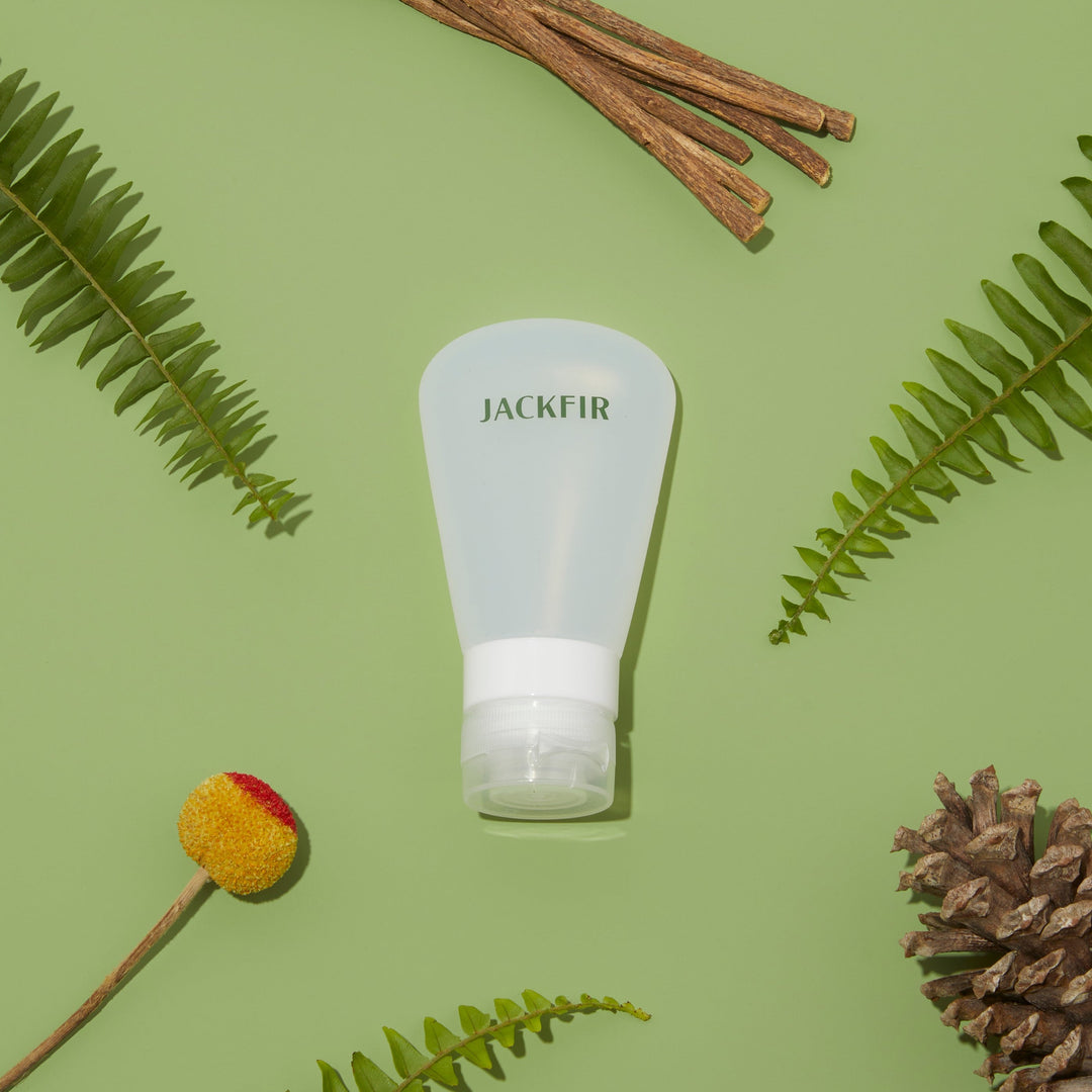 Jackfir TSA-Sized Travel Tube standing upright surrounded by fern fronds, twigs, pinecone and yellow craspedia flower