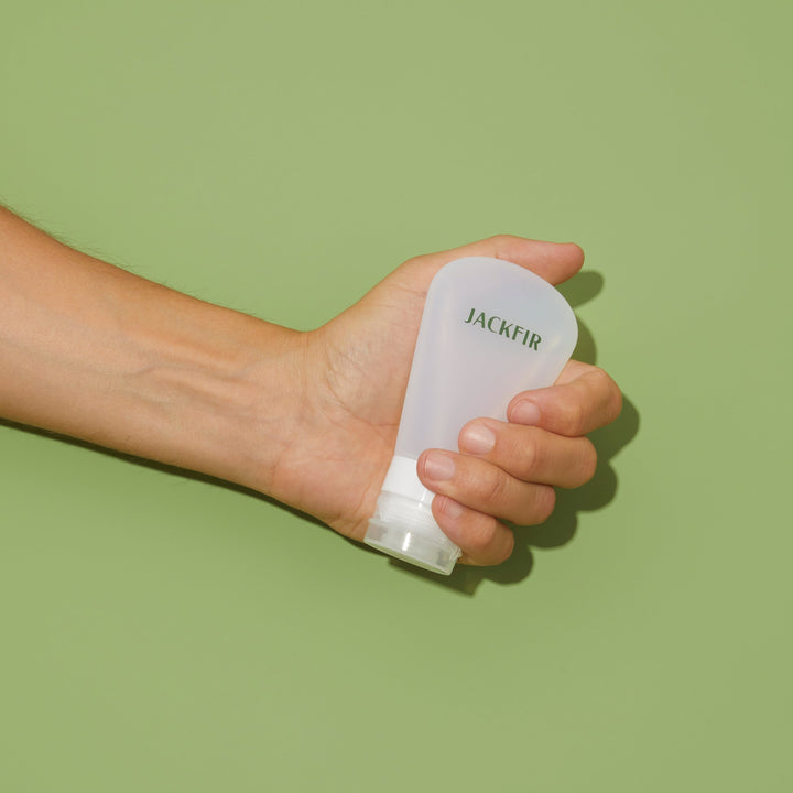 Hand holding Jackfir TSA-Sized Travel Tube in translucent white silicone with clear squeezable base